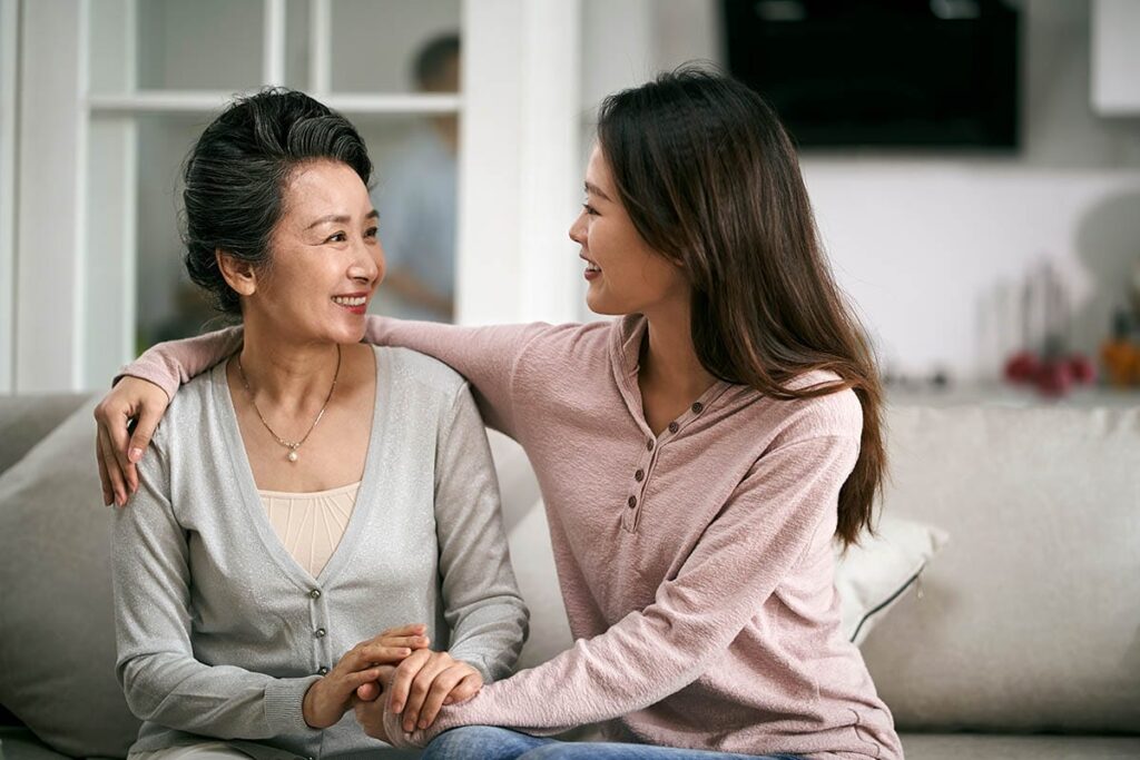 Woman sits on couch with arm around her mother, trying to prepare her for independent living