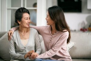 Woman sits on couch with arm around her mother, trying to prepare her for independent living