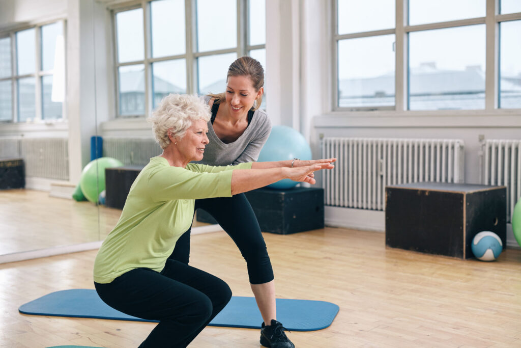 Woman squats with therapist during senior physical therapy techniques