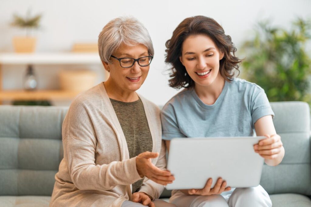 Woman shows her senior mom a laptop so she can learn about technology and communication in senior living